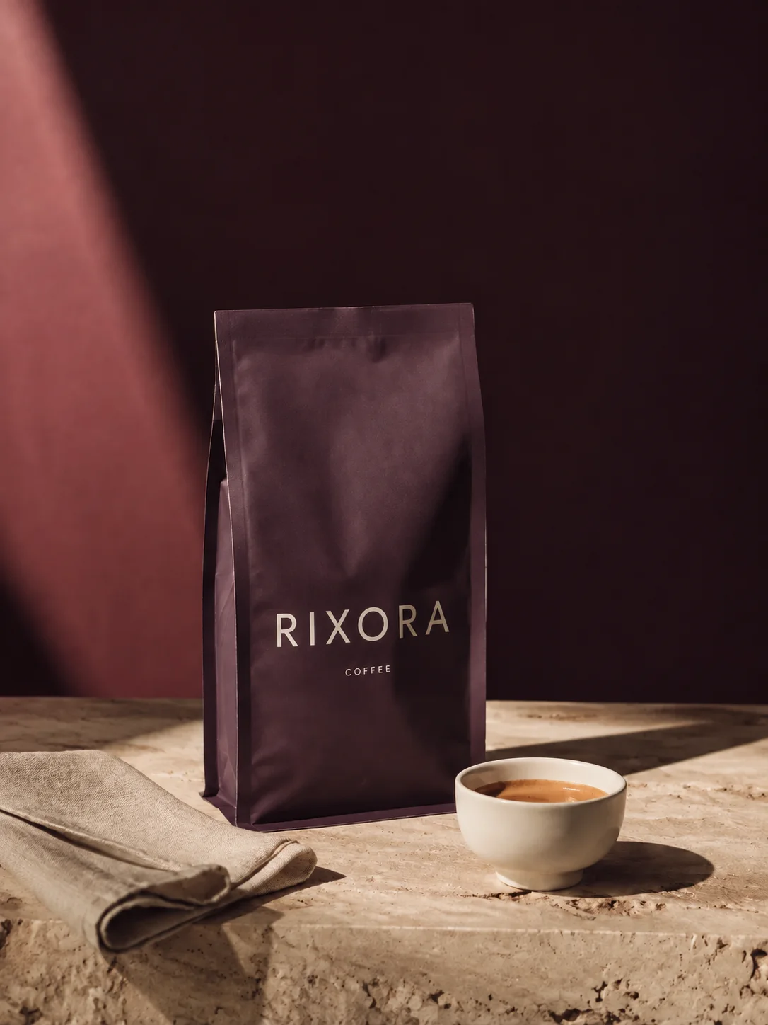 RIXORA-branded coffee packaging beside a white espresso cup in warm sunlight